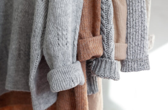 Pastel warm knitted clothes sweater hanging in the closet. Cozy autumn and winter wardrobe.