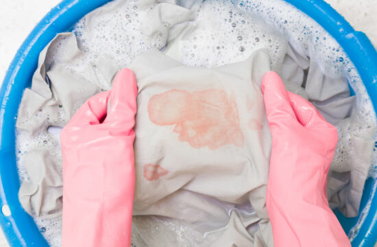 A person with gloves on trying to handwash a shirt with blood stains on it