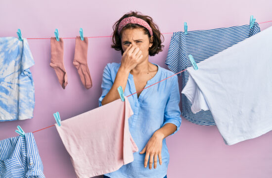 A woman holding her nose in front of smelly clothes.